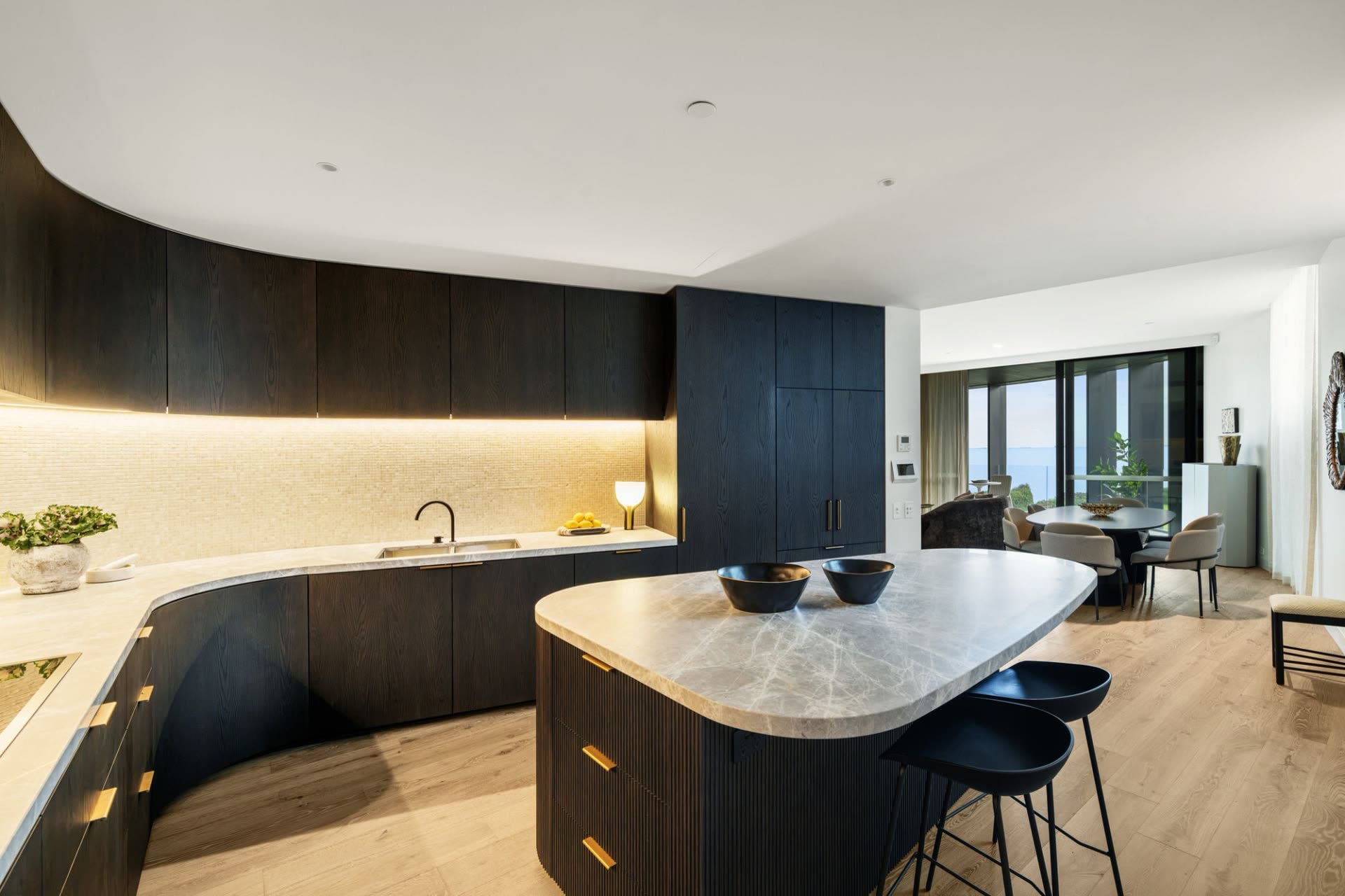 Kitchen with a curved marble island bench and dark joinery